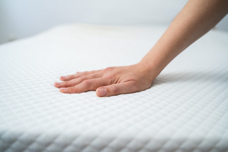 A hand feeling the firmness of a mattress